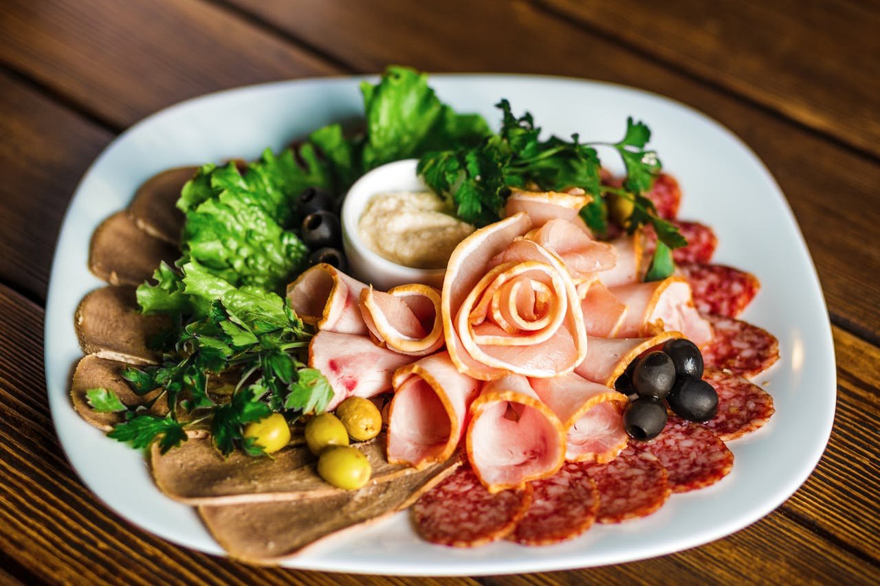 A vibrant assortment of cold cuts on a plate, garnished with olives and fresh greens, perfect for a party.